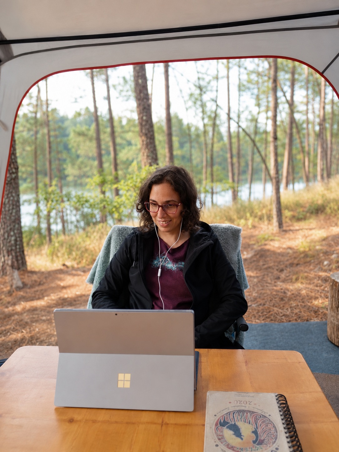 Eugénia a trabalhar no computador numa tenda, junto a uma floresta de pinheiros