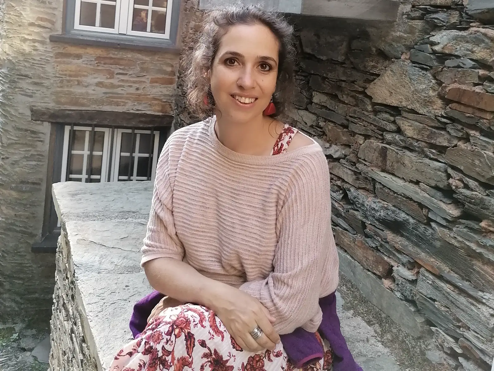 Eugénia Amaro, psicóloga, sentada junto a uma parede de xisto, em retrato de luz natural.