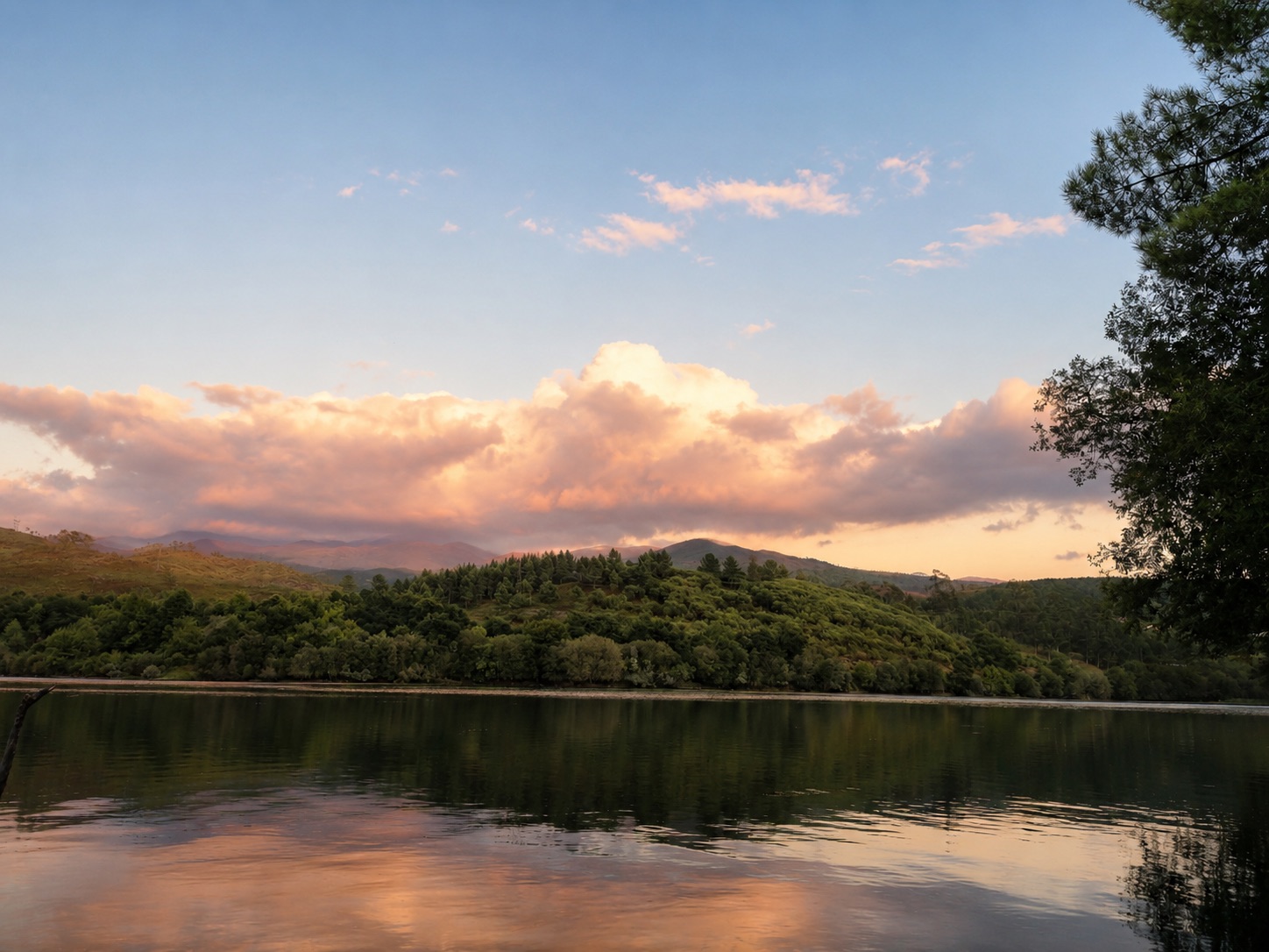 Paisagem ampla ao fim da tarde, com água a espelhar o céu rosado e colinas arborizadas