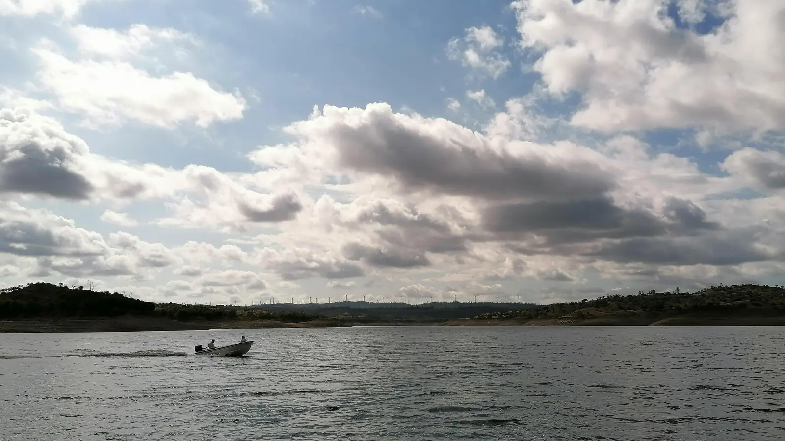 Lago largo sob um céu carregado de nuvens, com uma pequena embarcação ao longe.